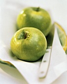 Zwei Granny Smith Äpfel auf Tuch mit Messer