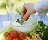 A Hand Dipping Broccoli into Vegetable Dip