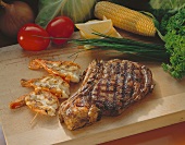 Prime Rib Steak mit Garnelenspiess auf Schneidebrett; Gemüse