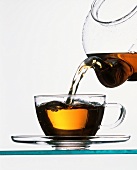Tee wird aus Glaskanne in Glastasse gegossen
