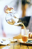 Tee aus Kanne in ein Glas einschenken