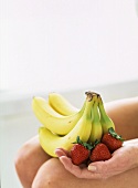 Hand hält Bananen und Erdbeeren auf den Knien