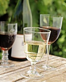 Drei Weingläser vor Weinflasche auf Holztisch im Freien