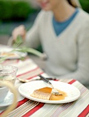 A slice of baked custard with caramel sauce in a table; a woman in the background