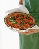 Woman serving tomato tart with basil in the baking dish