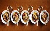 Five plates with chicken dishes and four white wine glasses