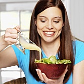 Junge Frau giesst Salatdressing über Blattsalat