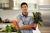 A Man Holding A Bunch of Carrots and a Bunch of Red Swiss Chard