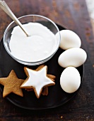 A Bowl of Icing with Star Shaped Cookies and Three White Eggs