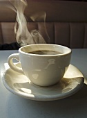 Dampfender schwarzer Kaffee in weisser Tasse
