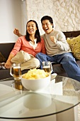 Couple on sofa watching television with crisps and beer
