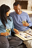 Couple on sofa drinking white wine & looking at photo album