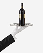 A Gloved Hand Holding a Silver Tray with a Bottle of Red Wine