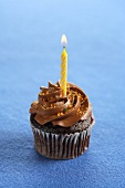 A Chocolate Cupcake with Chocolate Frosting, Colored Sprinkles and a Lit Yellow Candle