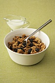 A Bowl of Granola with Raisins, Spoon and a Pitcher of Milk