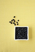 Black Beans in a Square White Bowl and on a Yellow Background