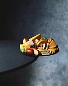 A fruit and cheese tray hanging off the edge of a table