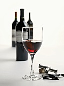 A Glass of Red Wine with Corkscrew, Cork and Wine Bottles