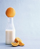 A Glass Bottle of Milk with Whole and Sliced Oranges
