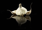 Garlic Bulb with Two Garlic Cloves on Black Surface Showing Reflection
