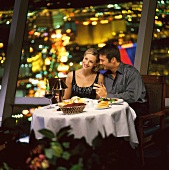Pärchen in Restaurant, im Hintergrund Stadt bei Nacht