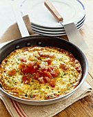 Frittata in a Skillet Topped with Fresh Tomatoes; Stack of Plates with a Spatula