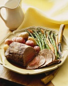 Partially Sliced Pork Roast on a Platter with Asparagus and Potatoes, Serving Fork