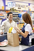 Kassiererin im Supermarkt füllt Lebensmittel in Papiertüte