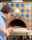 Pizza baker taking pizza out of the oven
