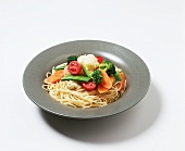 Spaghetti mit Gemüse auf Teller vor weißem Hintergrund