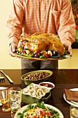 Man Holding Whole Roasted Thanksgiving Turkey on Platter Above Set Thanksgiving Table