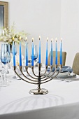 Manora with Lit Blue Candles on a Dining Table Set for Hanukkah