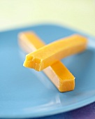 Two Cheddar Cheese Sticks on a Blue Plate, One Bitten