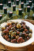 Marinierte Oliven auf Teller, dahinter Olivenölflaschen