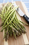 Many Organic Asparagus Spears on a Cutting Board with a Knife