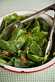 Tongs in a Serving Bowl of Spinach Salad with Bacon Dressing