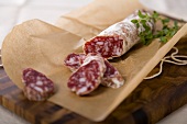 Partially Sliced Stick of Salami on Brown Paper; Cutting Board