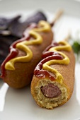 Two Corn Dogs with Mustard and Ketchup; One Bitten