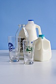 Two Plastic Containers of Milk with an Empty Bottle and Two Empty Glasses