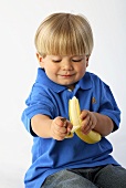 Ein sitzender kleiner Junge schält eine Banane