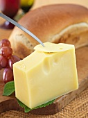 Ein Stück schweizer Käse, Messer, Brot und Weintrauben