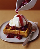 Pouring Fruit Sauce Over Waffle with Ice Cream