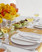 Gedeckter Tisch mit Salat, Weißwein und Blumenstrauss