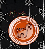 Black Cat Cookie Cutter on Orange Plate on Halloween Table Cloth