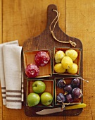 Various plums in bowls on a chopping board