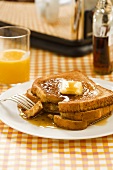 French Toast Stacked on a Plate with Maple Syrup and Butter; Fork