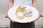 Woman Holding a Plate of Assorted Cheeses
