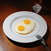 Two Over Easy Eggs on a Plate; Fork and Bottle of Tabasco