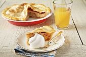 A slice of apple pie with whipped cream; apple pie in baking dish and a glass of apple wine
