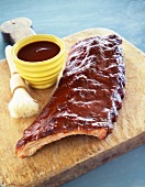 Slab of Barbecue Ribs on a Cutting Board with a Bowl of Sauce and Basting Brush